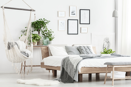 Patterned bedding on king-size bed and hammock above white fur in simple bedroom with posters